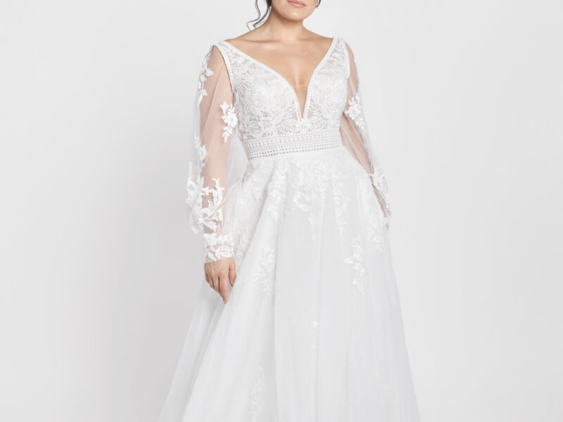 Charming bride to be wearing a long sleeve lace wedding dress with a deep v cut neckline, belted bodice and floral detailing on the skirt.