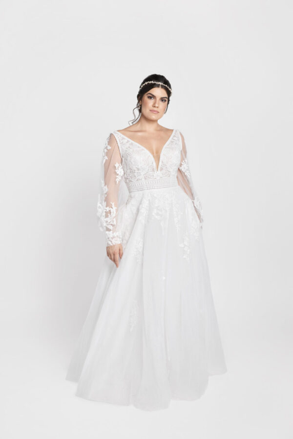 Charming bride to be wearing a long sleeve lace wedding dress with a deep v cut neckline, belted bodice and floral detailing on the skirt.