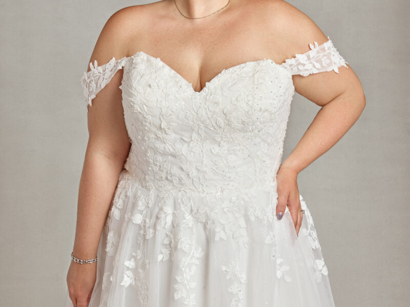 Plus size model wearing her wedding dress with tulle skirt and floral detailing on the bodice and off the shoulder sleeves.