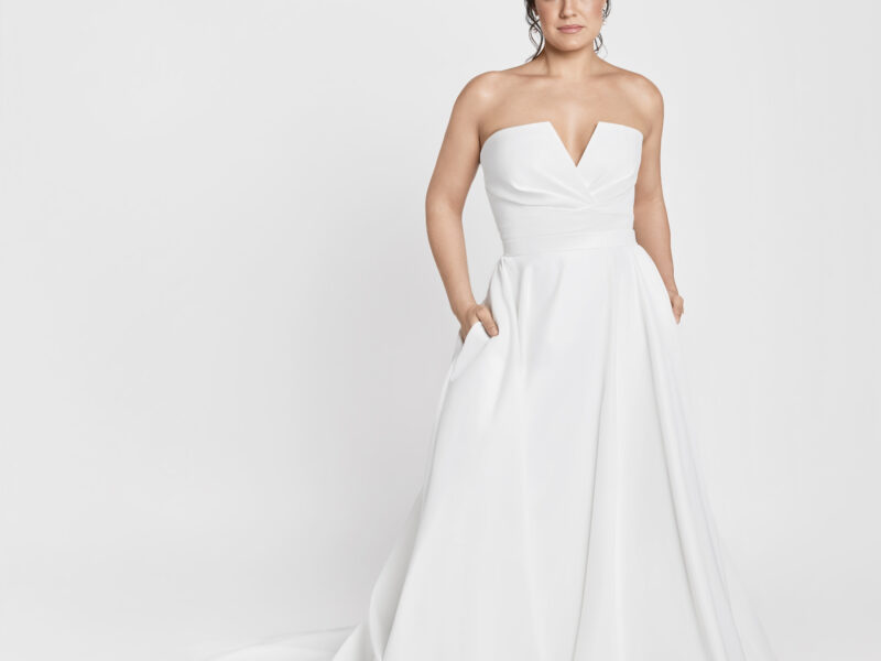 Confident bride modeling her simple, sleeveless wedding dress with a full skirt and hidden pockets.