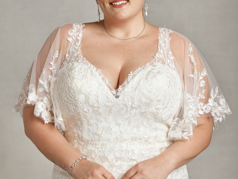 Curvy bride to be wearing a wedding dress with sleeves. The dress has small floral detailing on the bodice, sleeves and skirt.