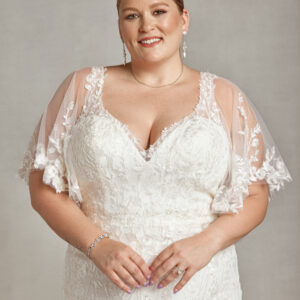 Curvy bride to be wearing a wedding dress with sleeves. The dress has small floral detailing on the bodice, sleeves and skirt.