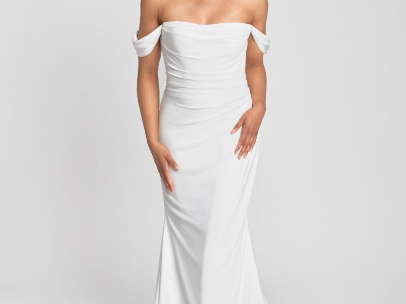 A smiling bride to be wearing an off the shoulder sleeve wedding dress with a ruched bodice and simple skirt.