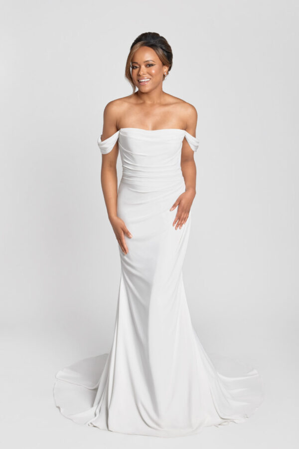 A smiling bride to be wearing an off the shoulder sleeve wedding dress with a ruched bodice and simple skirt.