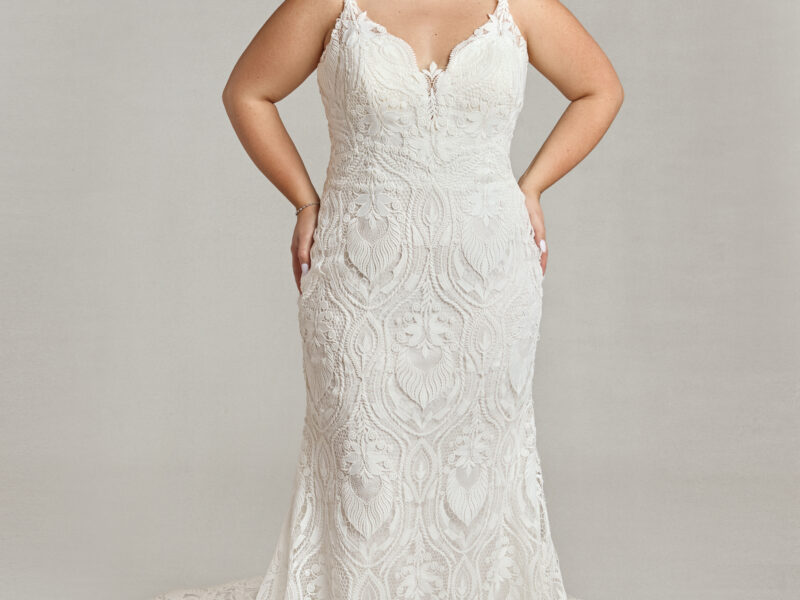 An art deco inspired wedding dress with unique lace pattern worn by a bored bride with her hands on her hips.