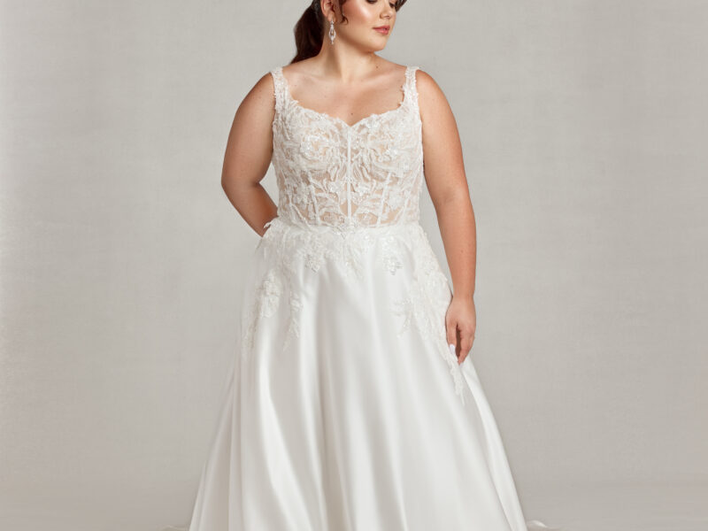 Confident plus size bride wearing a corseted wedding dress with see through bodice and shimmering, floral lace.