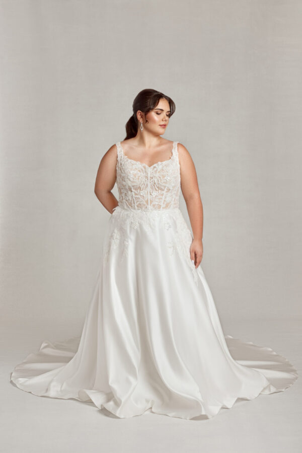 Confident plus size bride wearing a corseted wedding dress with see through bodice and shimmering, floral lace.