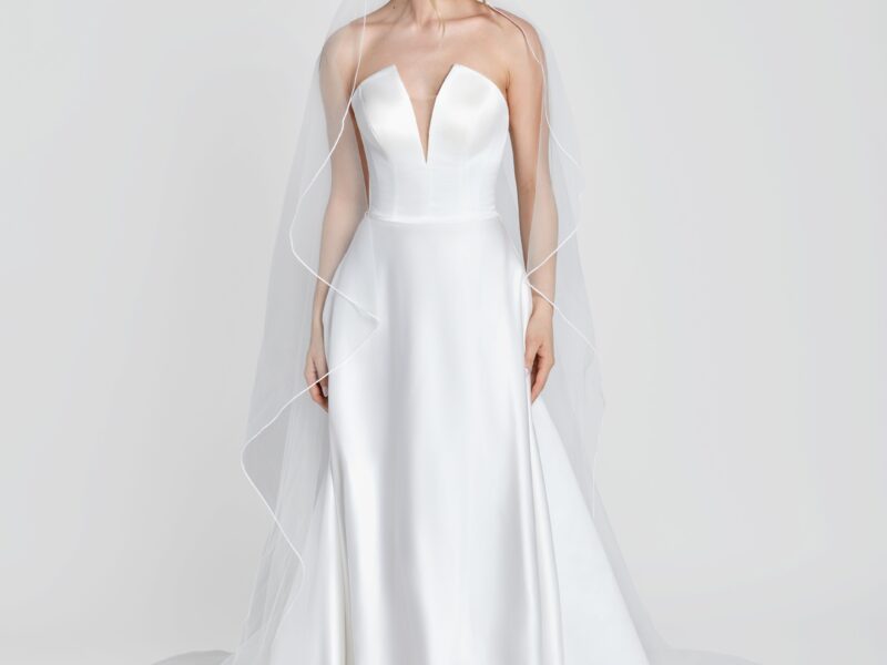 Simple wedding dress with a deep v cut neckline and simple, full skirt worn with a simple, long veil.