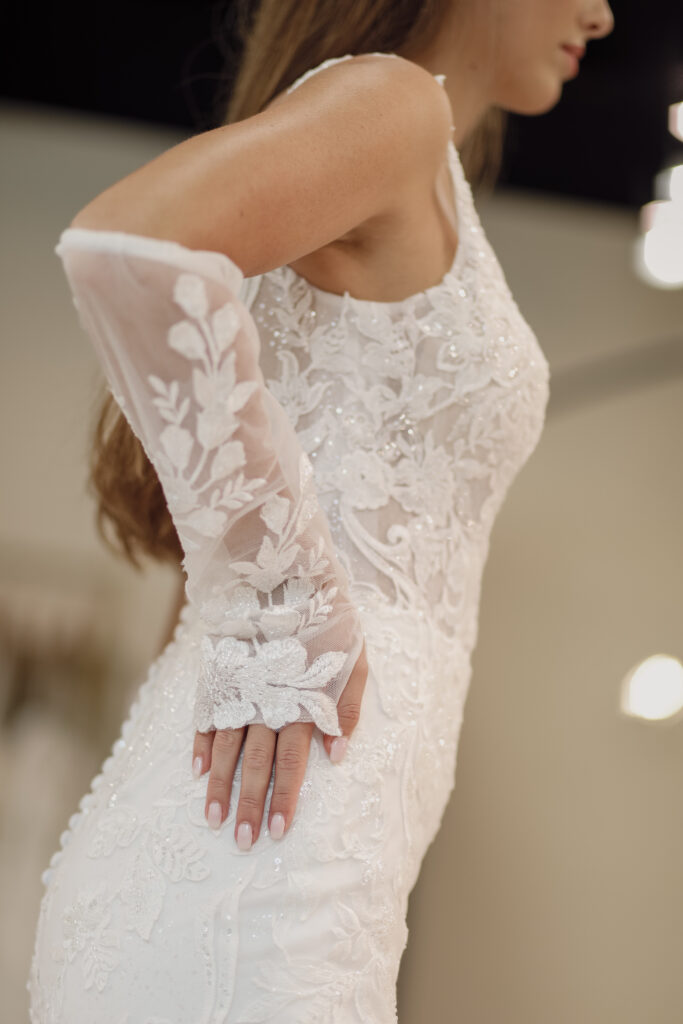 A close-up of a bride wearing a long-sleeved lace wedding dress with intricate floral embroidery.