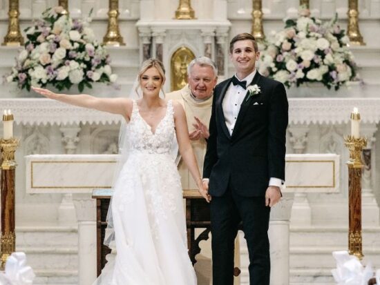 A bride and groom stand at the altar, beaming with joy after being pronounced married. The bride wears a lace wedding dress, and the groom is in a black tuxedo.