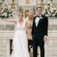 A bride and groom stand at the altar, beaming with joy after being pronounced married. The bride wears a lace wedding dress, and the groom is in a black tuxedo.