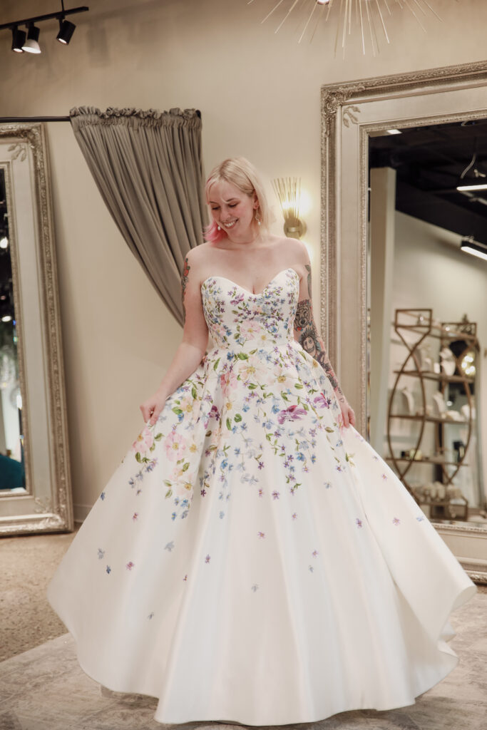 Happy bride twirling in a colorful floral wedding dress, enhancing the festive mood of the boutique.