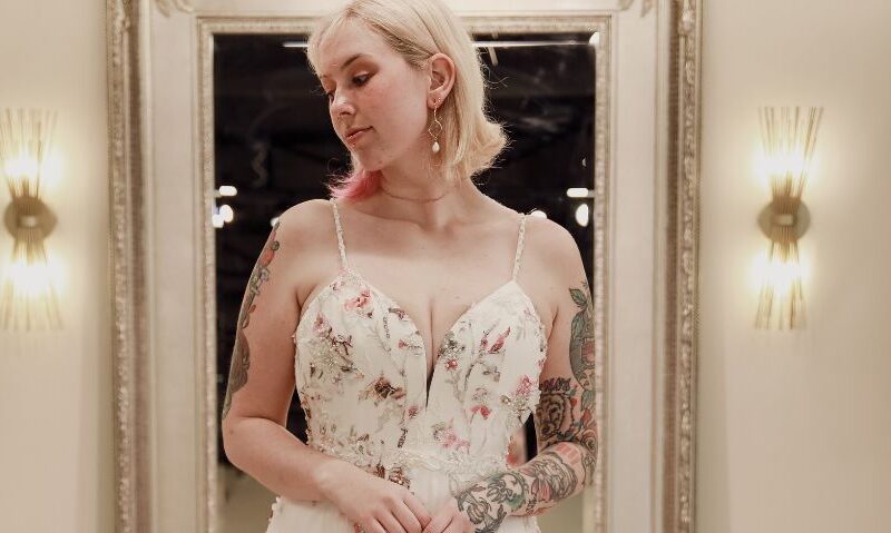 Close-up of a bride in a pastel floral gown, reflecting thoughtfully in a boutique mirror.