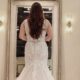 Rear view of a bride in a long white lace wedding dress, standing in front of a vintage mirror.