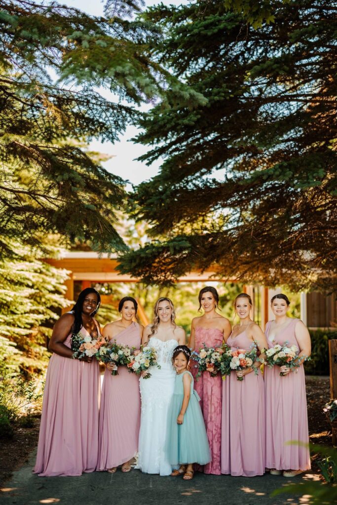 A bridal party and flower girl smiling at a Michigan wedding venue with orange, yellow, and white flower bouquets.