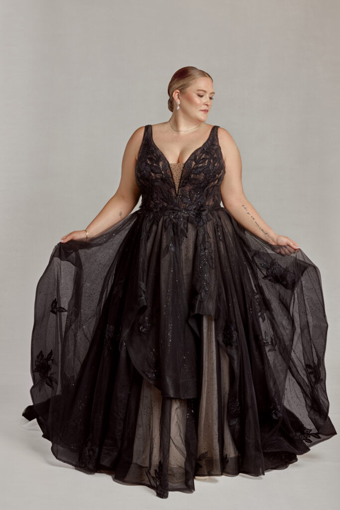 A bride wearing a plus-size black wedding dress in front of a plain gray background.