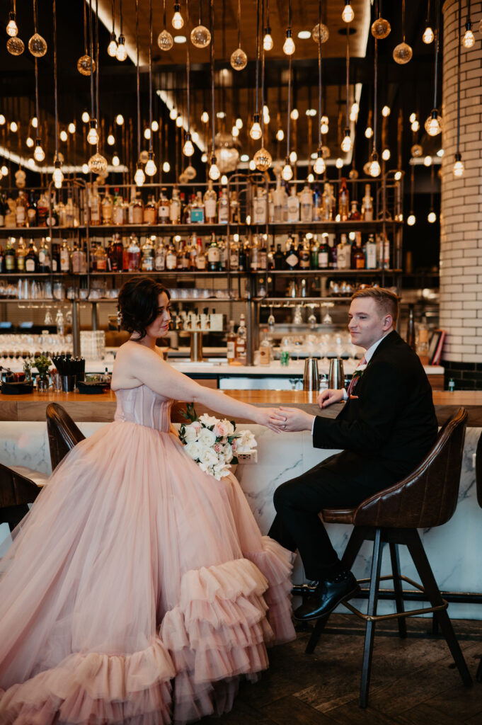 Bride in pink dress and groom at a chic bar during their wedding celebration.