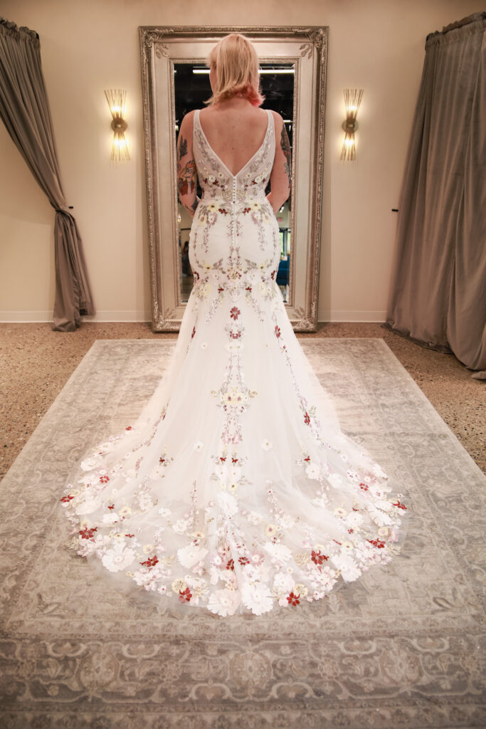 Bride in a colorful floral train wedding dress looking at her reflection in a mirror.