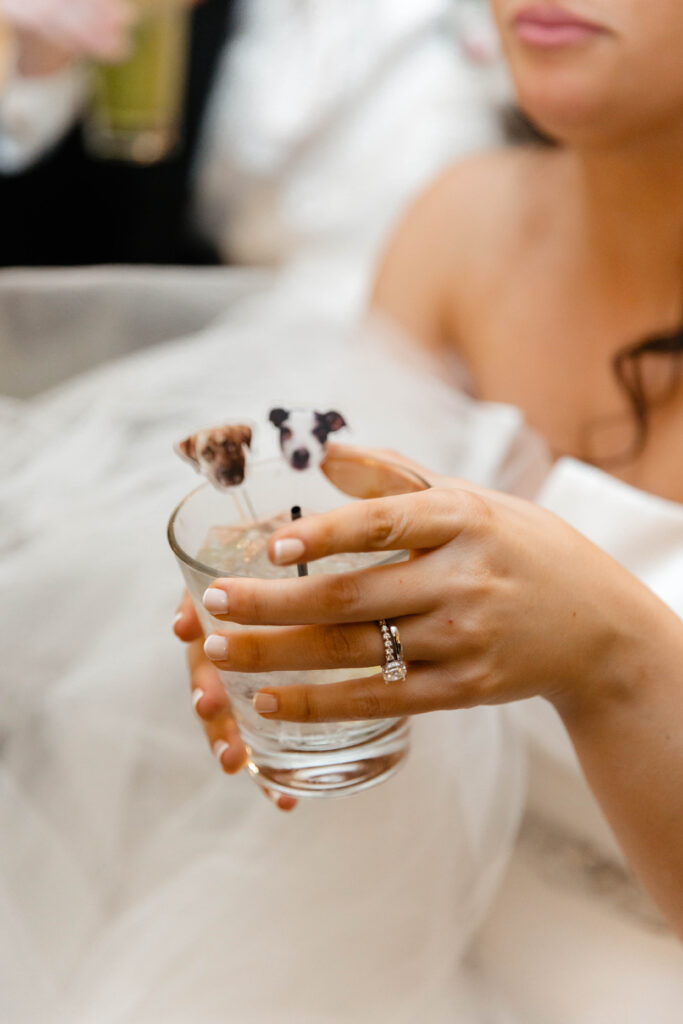 Close-up of a bride holding a cocktail with customized dog stirrers.