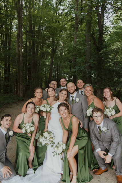 Bride and groomsmen in green, laughing in a lush forest setting.