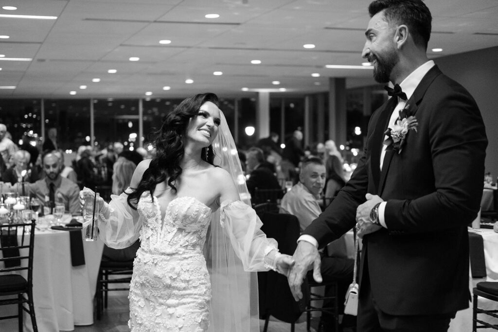 A bride and groom hold hands and smile at each other as they enjoy their wedding reception.