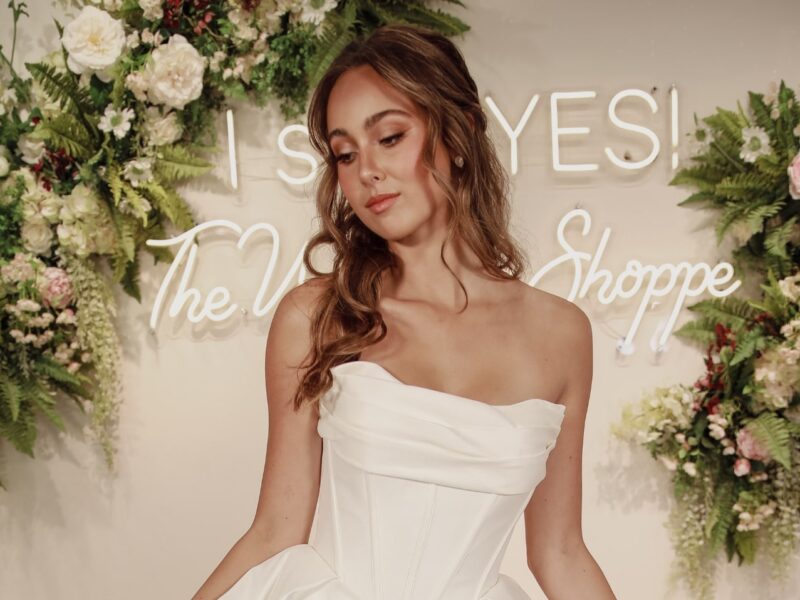 Bride posing under a floral arch in a chic off-shoulder basque gown.