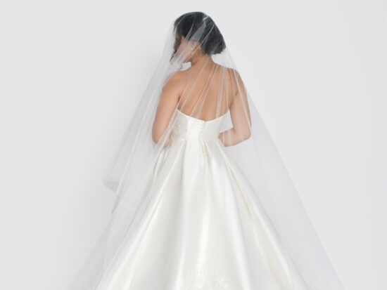 Bride viewed from behind, showcasing a long, flowing veil and satin wedding gown.