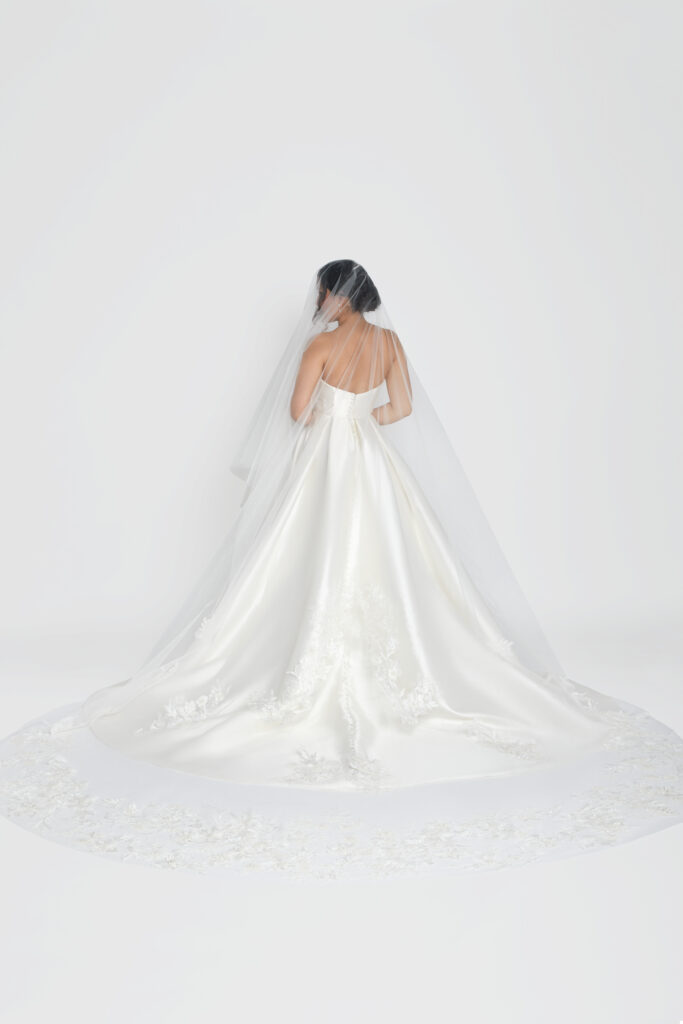 Full back view of a bride in a satin gown with an embroidered train and sheer veil.