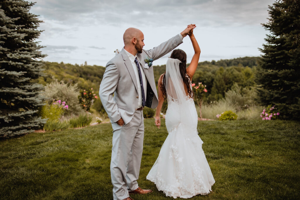 Couple dancing on a lush green lawn, bride in a detailed lace gown.