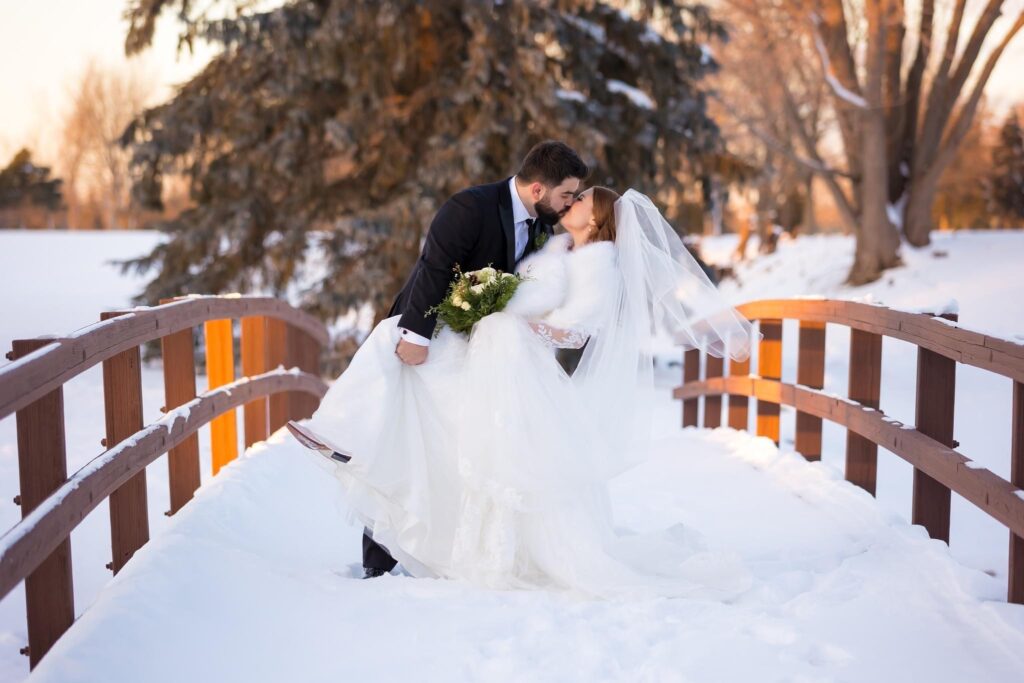 Couple kissing on a snowy bridge, bride in a flowing gown with a fur shawl.