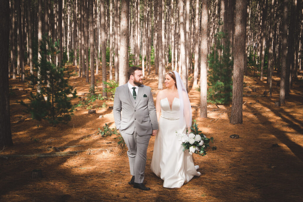 Couple walking hand-in-hand in a pine forest, bride in a white dress.