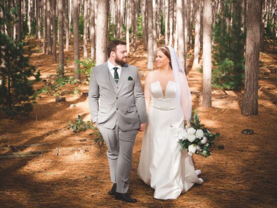 Couple walking hand-in-hand in a pine forest, bride in a white dress.