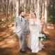 Couple walking hand-in-hand in a pine forest, bride in a white dress.