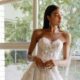 Elegant bride in a strapless lace gown with a high slit standing by a window.