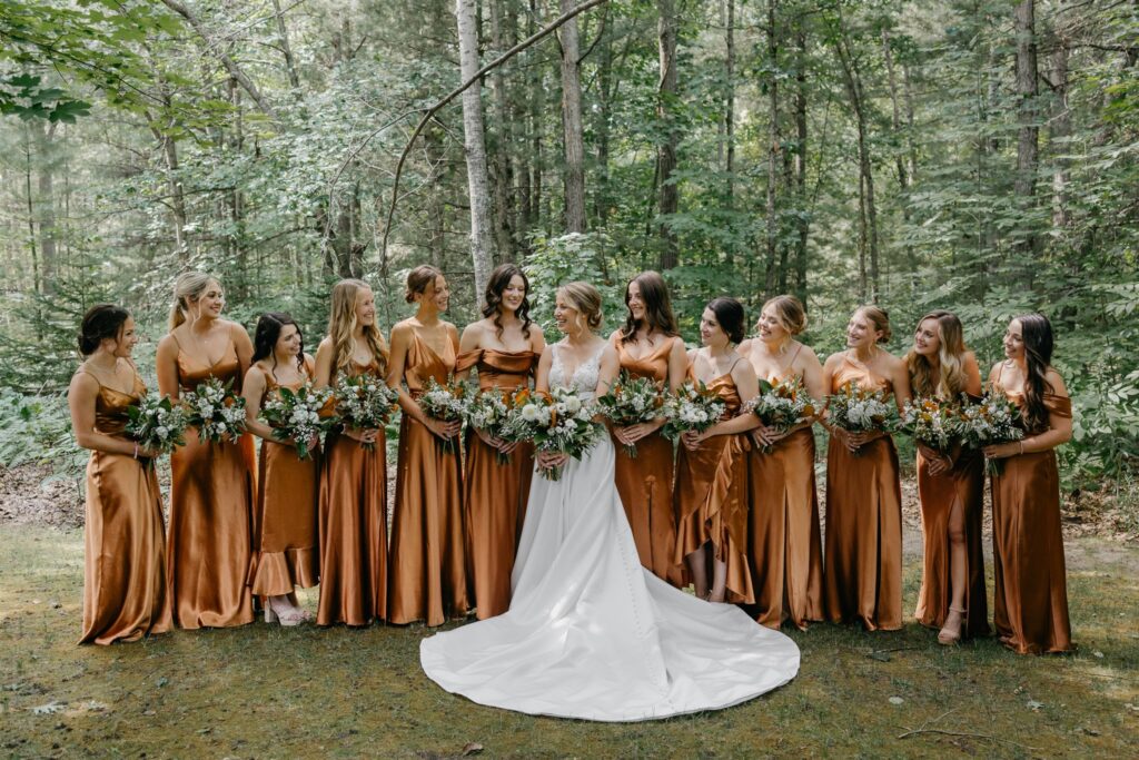 Bridal party in golden dresses in a lush forest, bride in a flowing white gown.