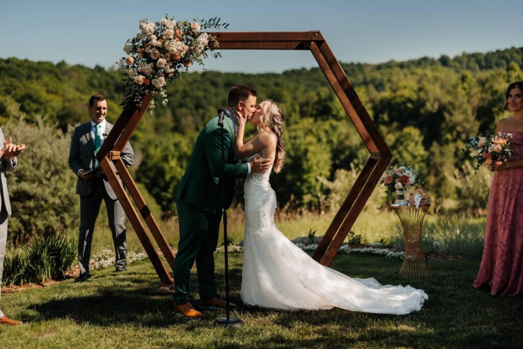 Bride and groom sharing a kiss in front of a wooden hexagonal archway adorned with flowers.