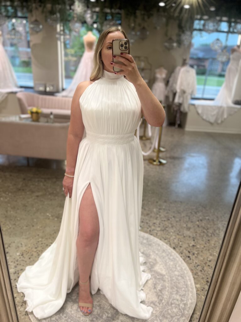 Confident bride taking a mirror selfie in a white halter-neck gown with a floor-length slit.