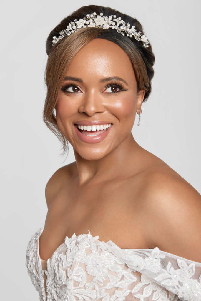 Smiling bride wearing a detailed tiara and diamond earrings, close-up portrait.