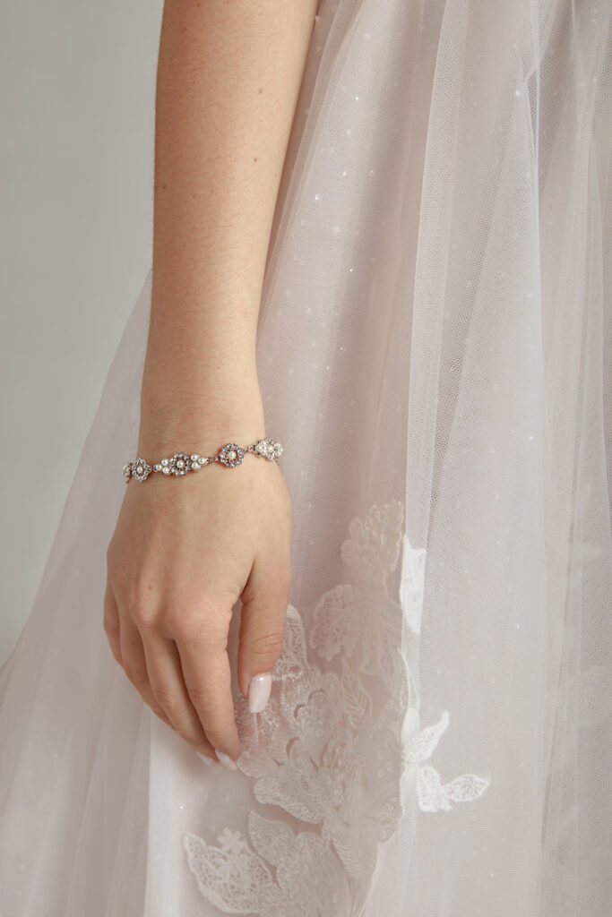 Bride showing a delicate, sparkling floral bracelet on her wrist, holding a veil.