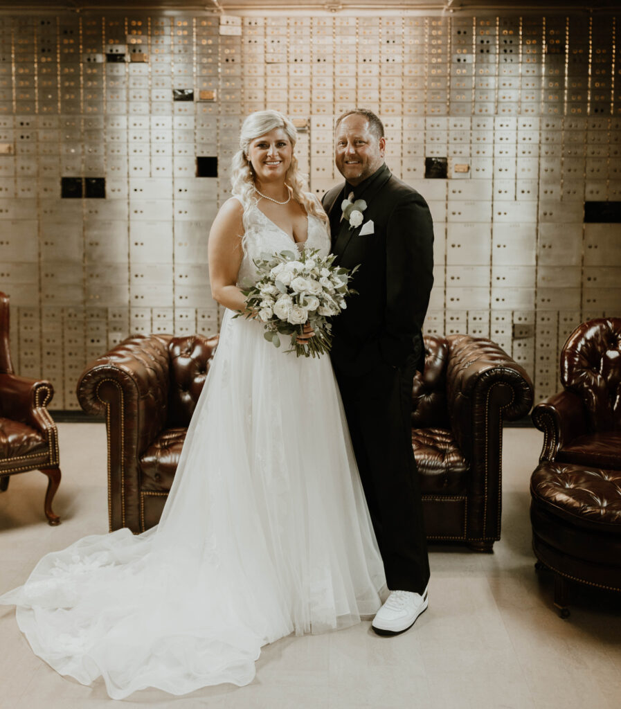 Bride and groom standing in an elegant room with historical vault detailing, smiling warmly.