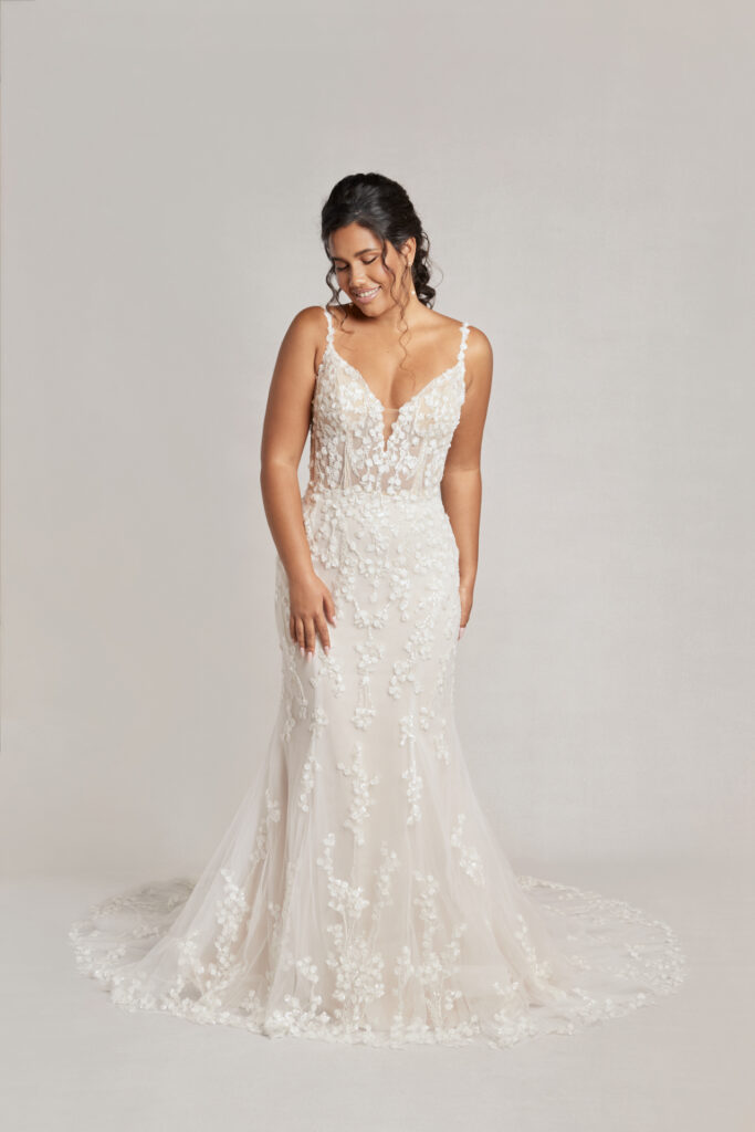 Smiling bride in an embellished white gown with deep V-neck, at a serene indoor setting.