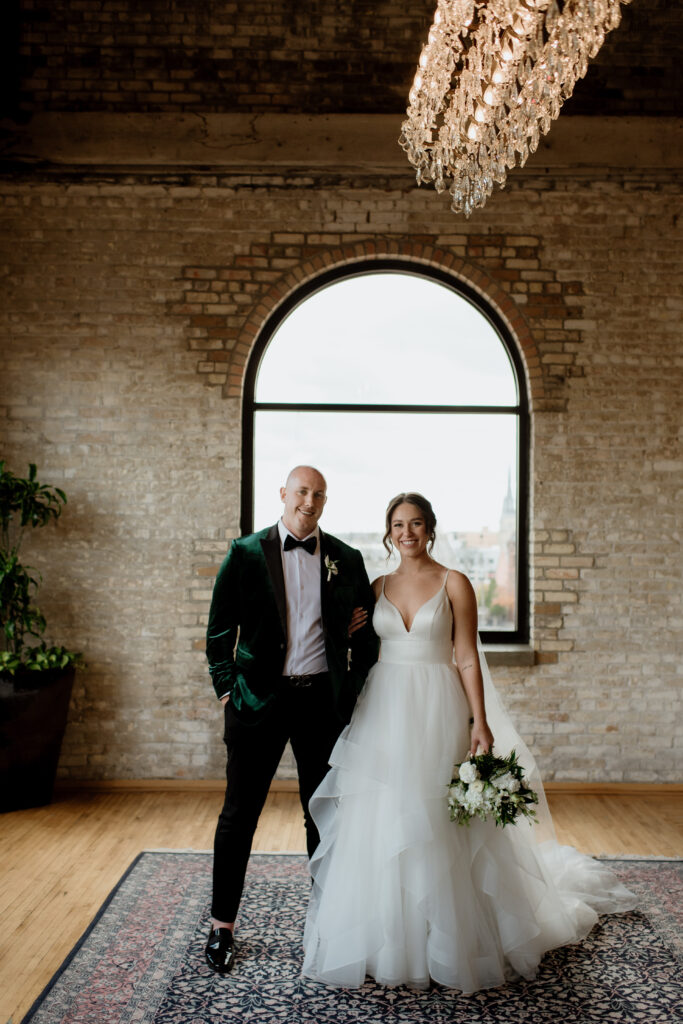 Newlywed couple posing in an urban loft with rustic brick and large windows, bride in flowing gown.