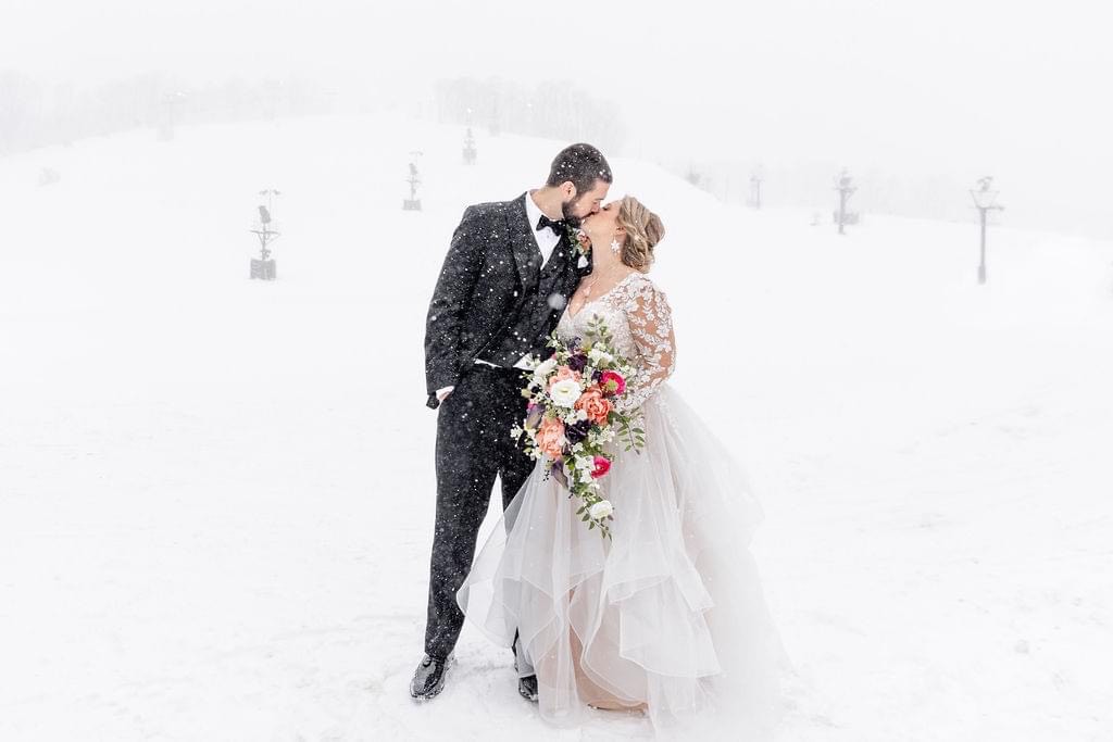 Bride and groom kissing in a snowy landscape, adorned in elegant wedding attire.