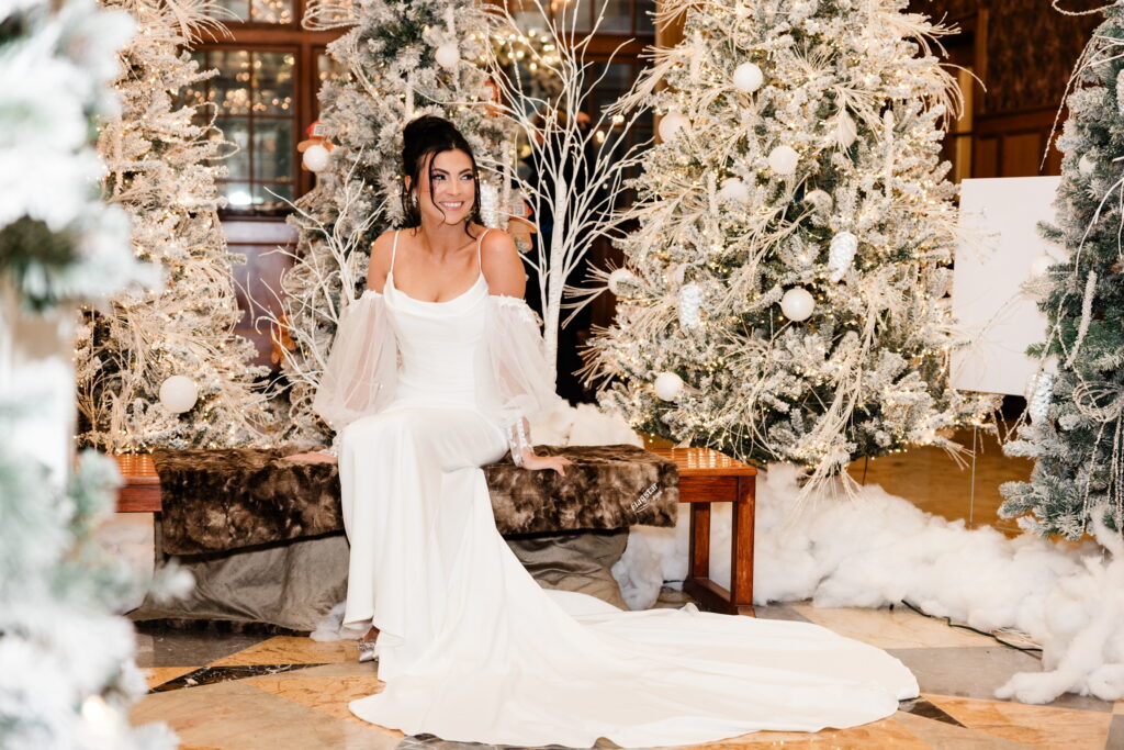 Bride seated elegantly among lavish winter-themed decorations, sparkling trees surrounding.