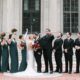 Bridal party celebrating with joy on the steps of William L. Clements Library, under clear skies.