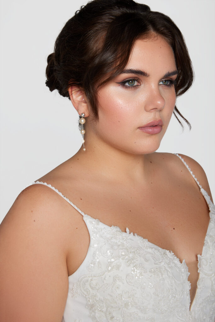 Bride wearing drop pearl earrings and a lace dress, showing a soft, natural makeup look and traditional bridal jewelry.