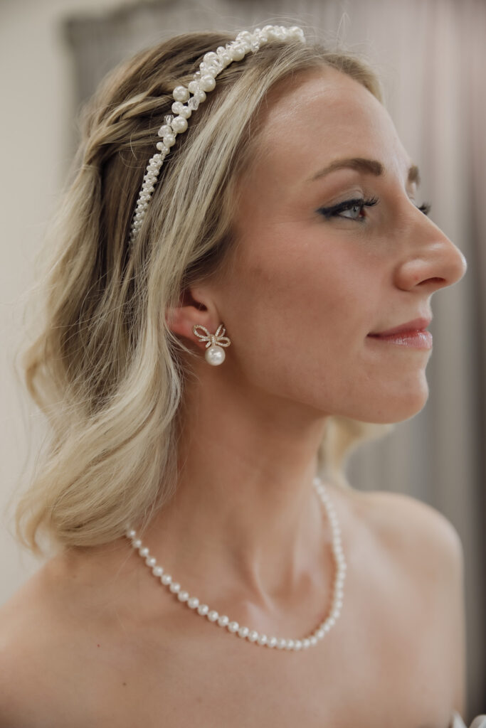 Bride wearing a classic pearl necklace and pearl-drop earrings with a twisted headband, exuding a traditional bridal style.