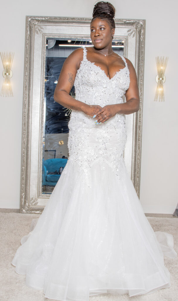 Bride in a fitted beaded gown, posing gracefully in front of a large ornate mirror, radiating confidence.