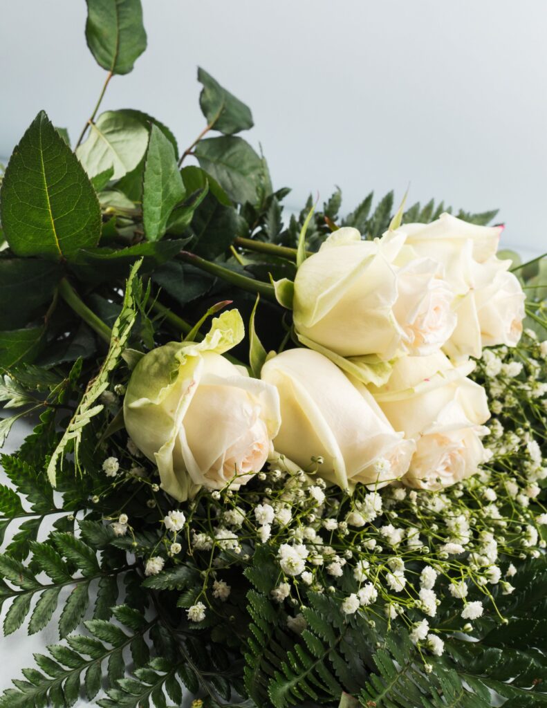 White roses and delicate baby's breath arranged with lush greenery for an elegant, classic bridal bouquet.