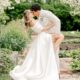 Bride and groom share a romantic kiss in a lush garden setting, with bride in elegant off-shoulder gown and long train.